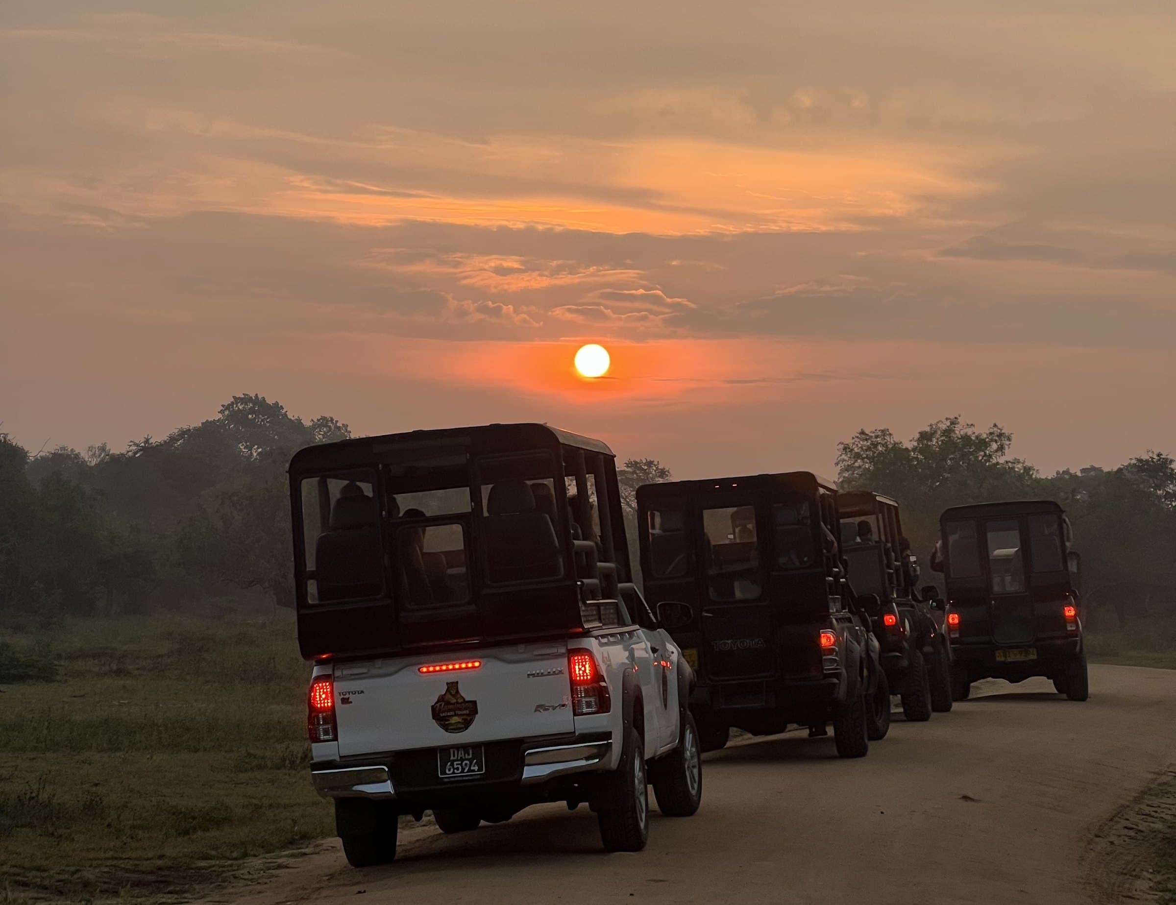 A convoy of safari jeeps driving into the sunset